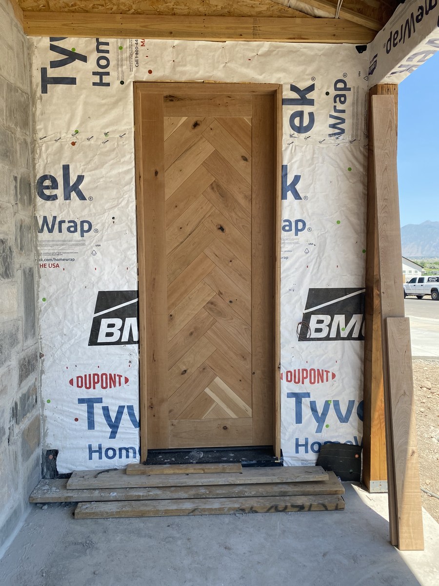 Wood entry door with a chevron pattern, pictured during construction